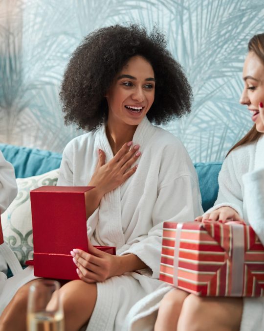 Contented brunette woman looking grateful while opening her holiday gifts with her best girlfriends